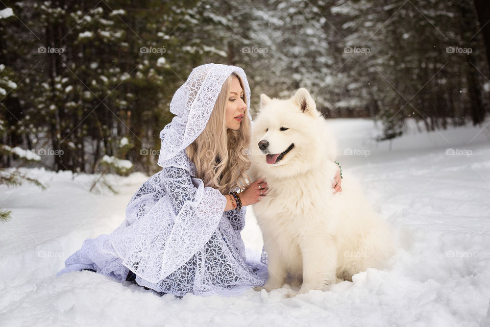 Beautiful young woman stroking her dog in snowy weather