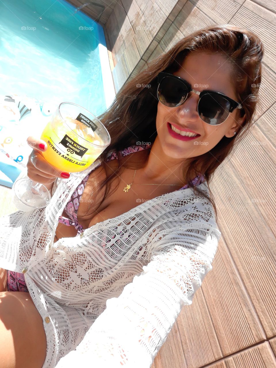woman at the edge of the pool with glass of drink in her hand.