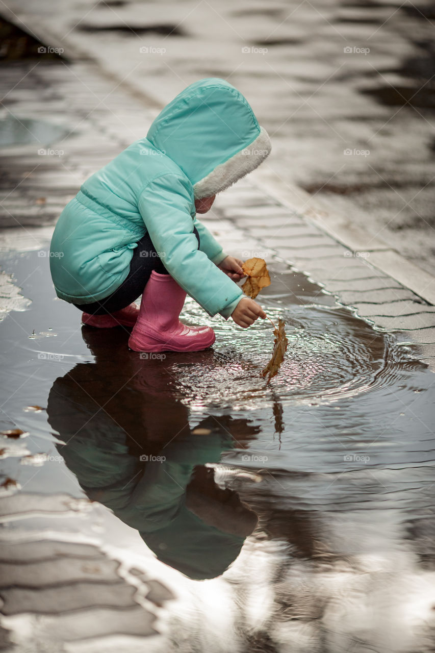 Little girl in rubber boots playing in puddle