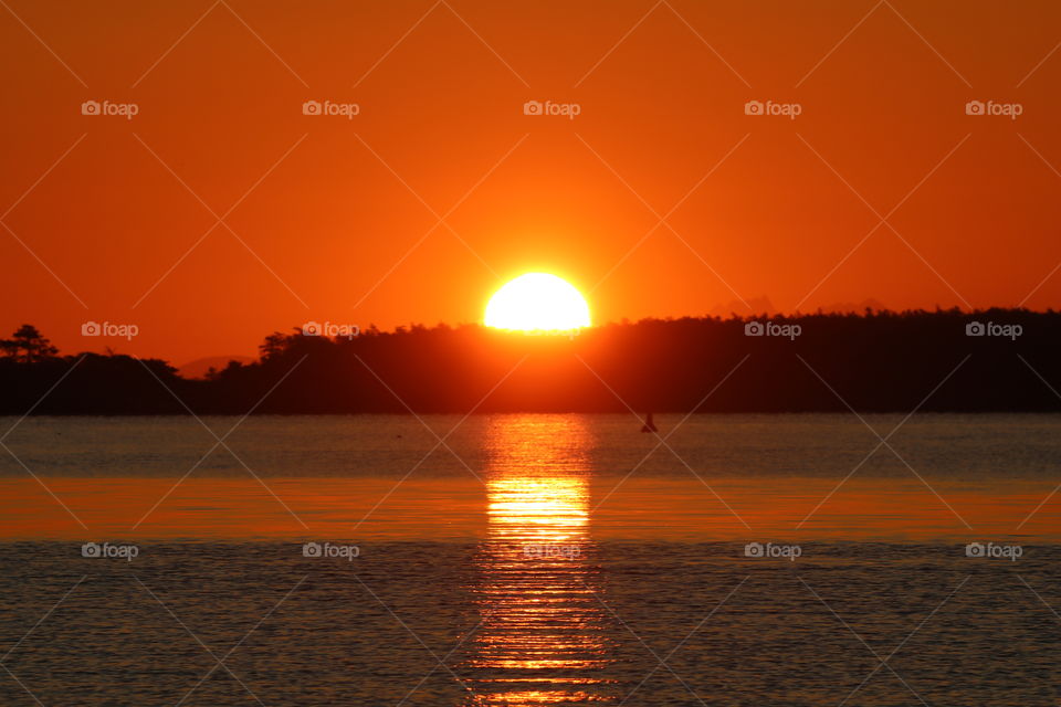 Sun popping up behind the mountain painting the sky orange and casting its reflection into the ocean