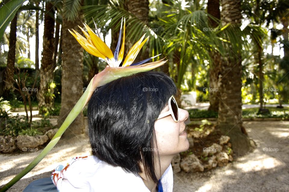 It is a purple and yellow flower. The flower is placed on the head of the model. The model also wears yellow glasses. A creative photograph.