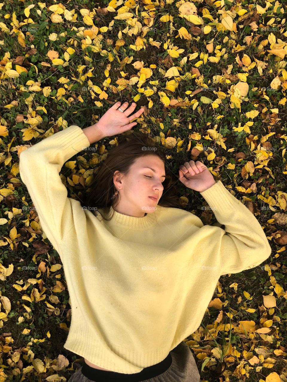 Girl in yellow sweater sleeping on a yellow leaves in autumn