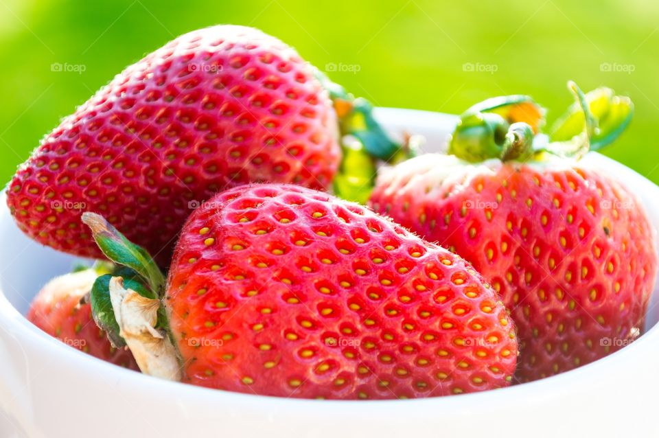 Strawberries in the sunlight. A bowl if strawberries backlit by the sun with a green background