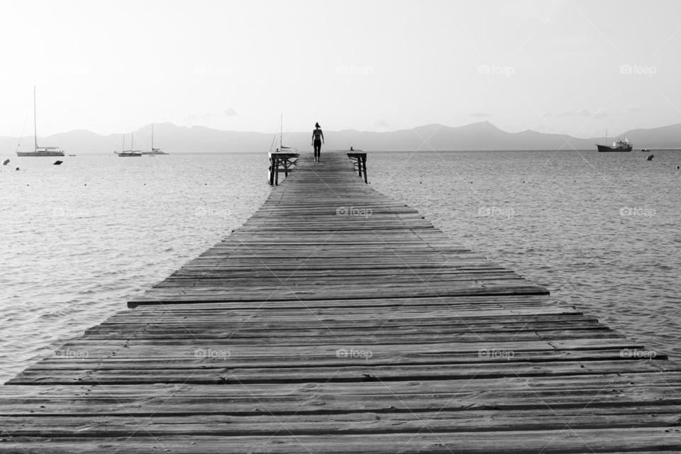 Woman walking on wooden pier in the ocean, black and white 