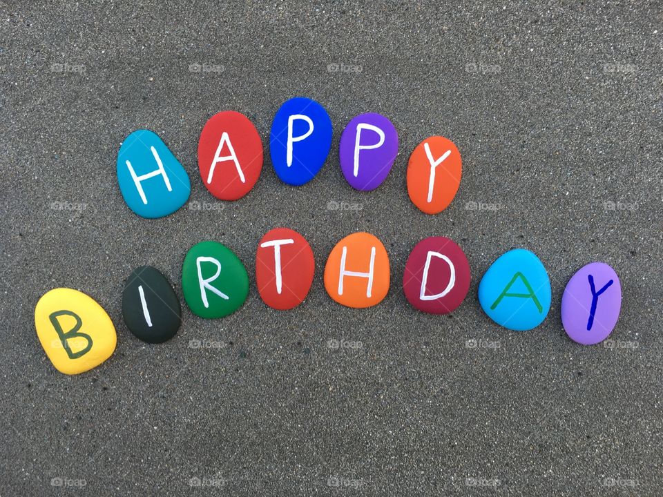 Happy Birthday on colored stone letters over black sand