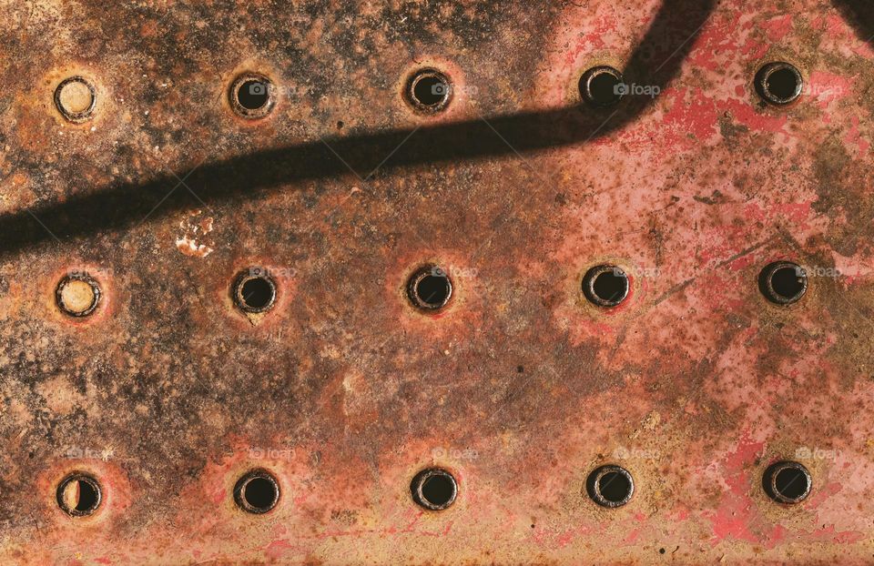 Circle pattern in rusty metal plate with dramatic sunlight and shadow