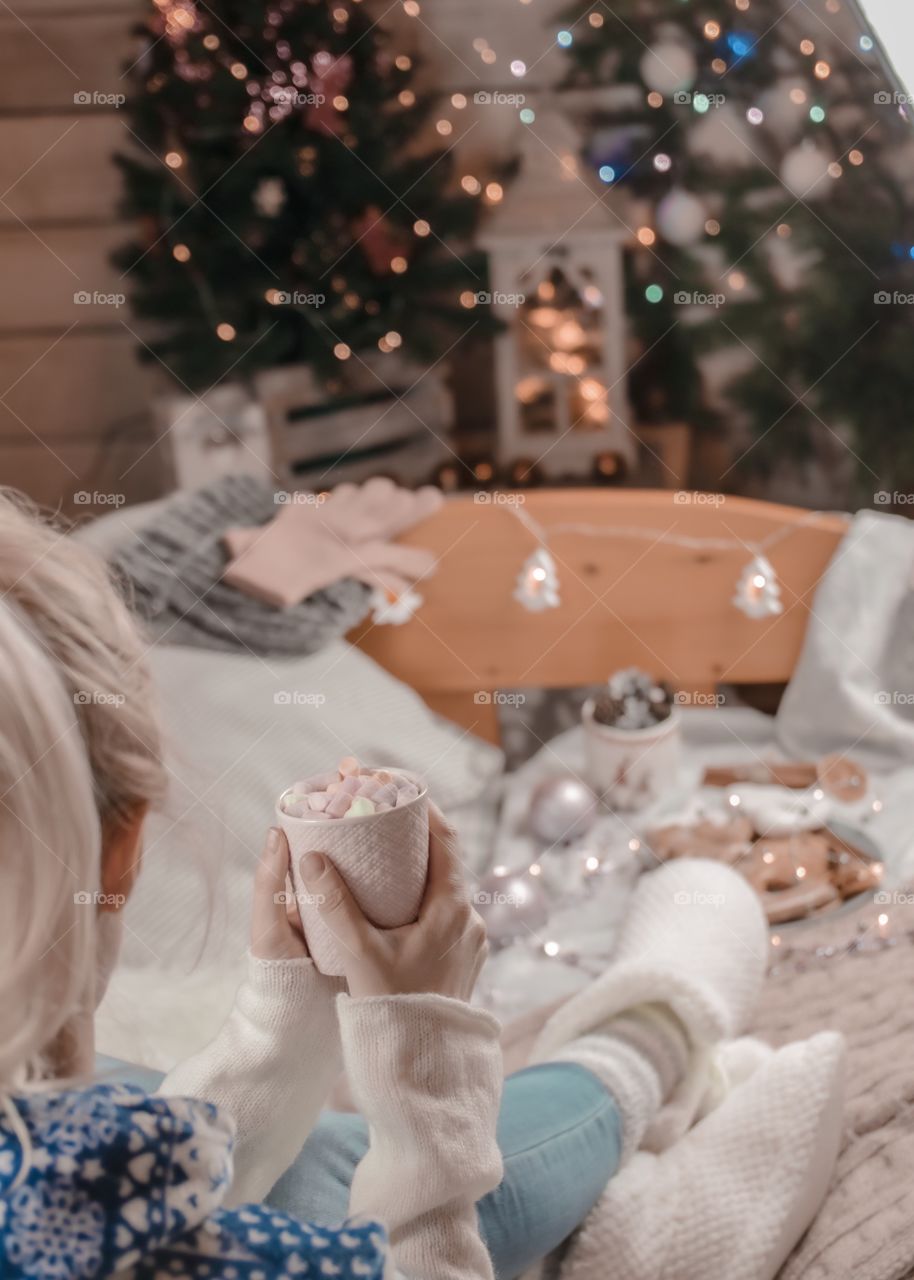 Cup with marshmallows in female hands on a background of Christmas decor