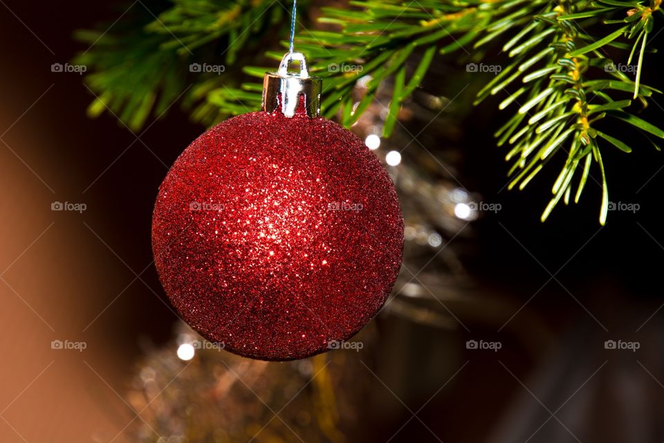 A red shiny and glittery christmasball hanging in the Christmas tree