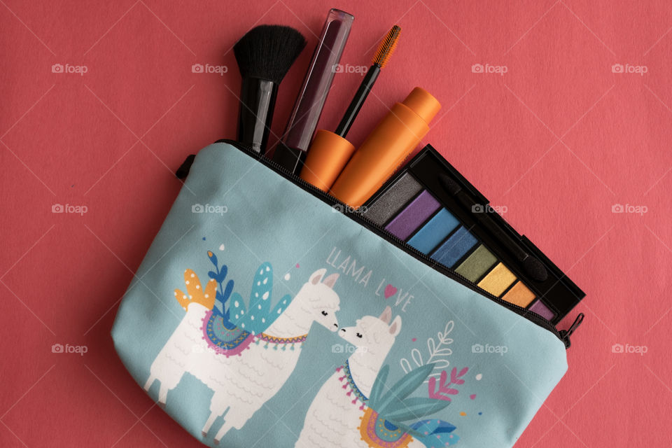 Looking down on a bright table top with various makeup items in a light blue pouch with llamas on it