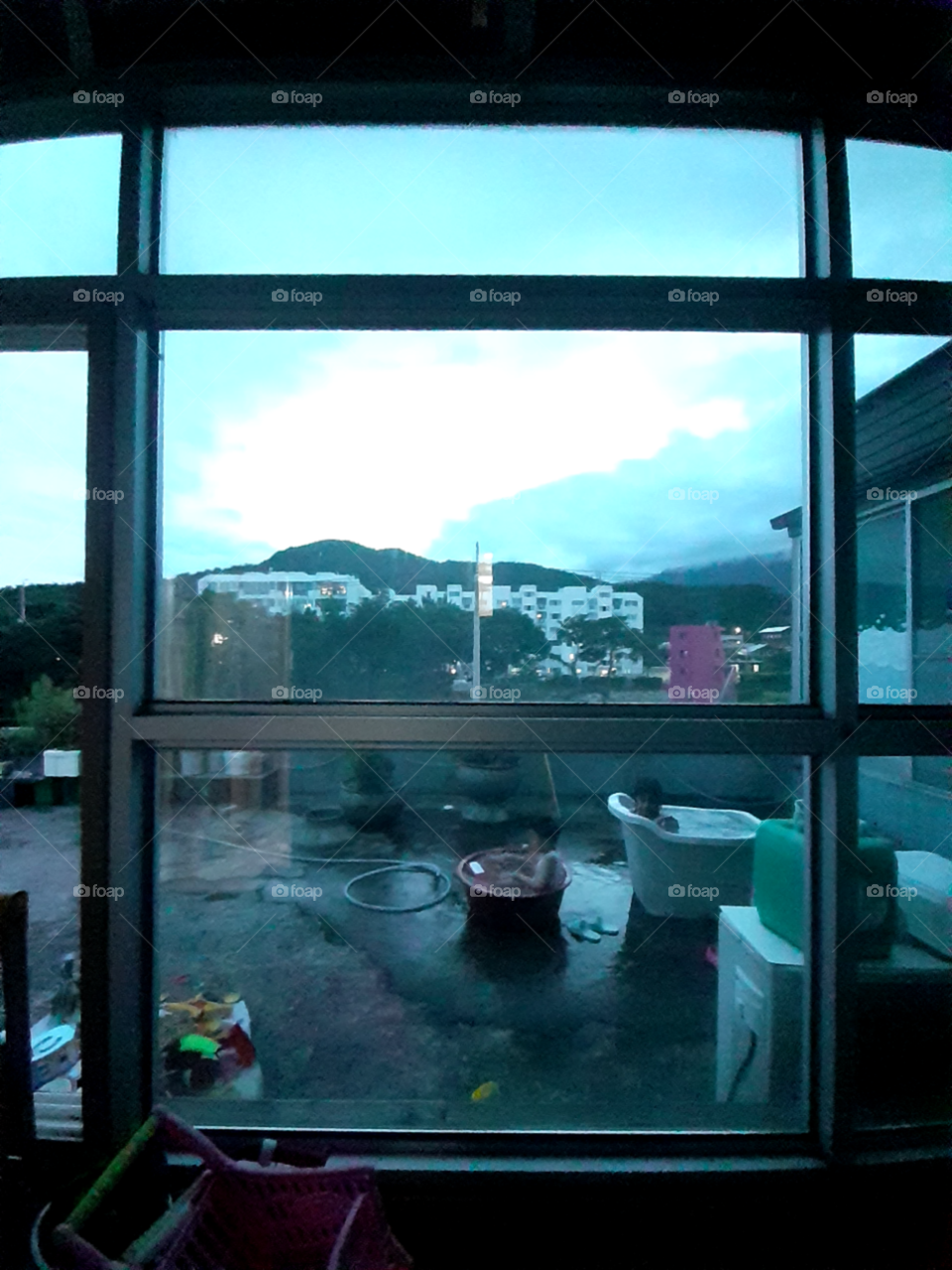 outside the children are playing water and doing swimming because of hot weather.  its quite dark because its after the sunset.