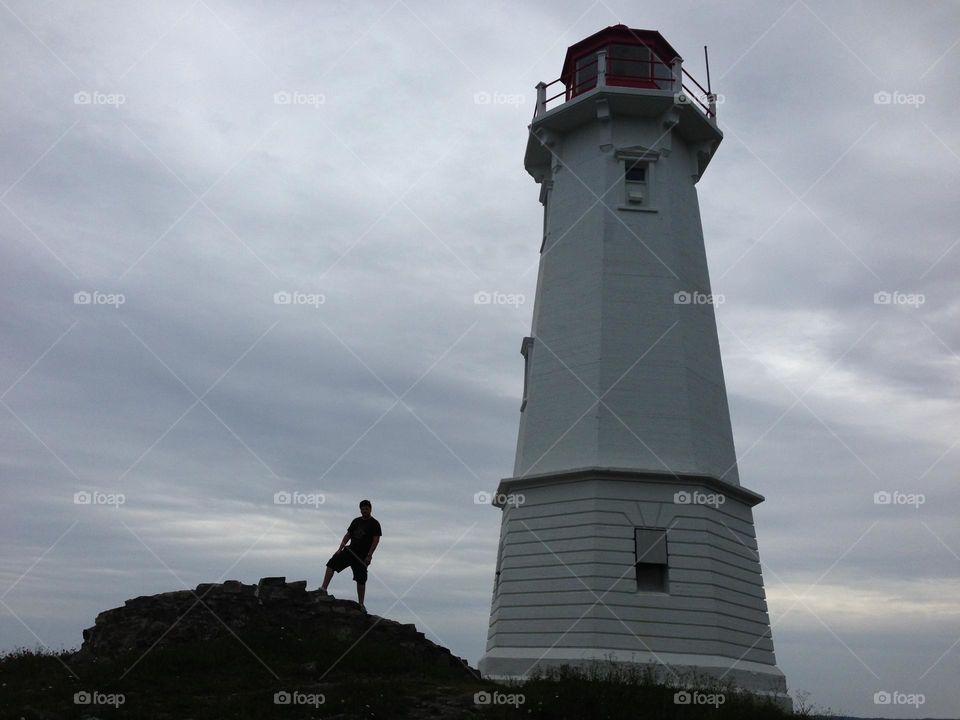 Sydney , Nova Scotia . Lighthouse on a cloudy day , man standing beside the lighthouse on a hill. 