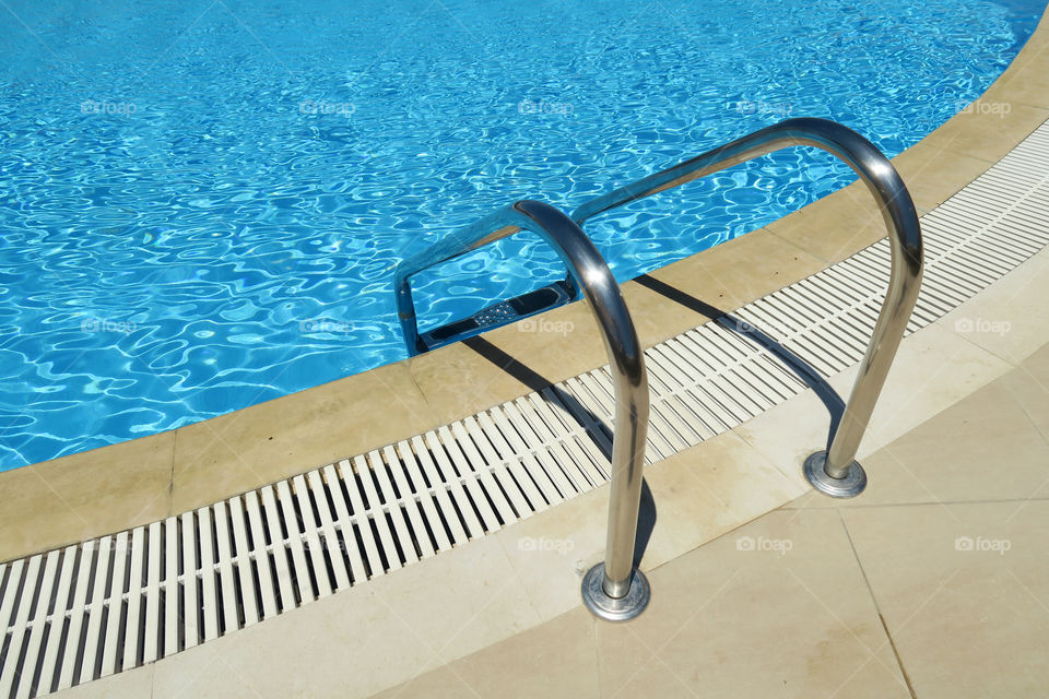 Outdoor swimming pool ladder. Grab bars metal ladder to a blue water pool.