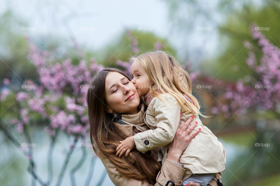 Little daughter kissing her mother outdoor 