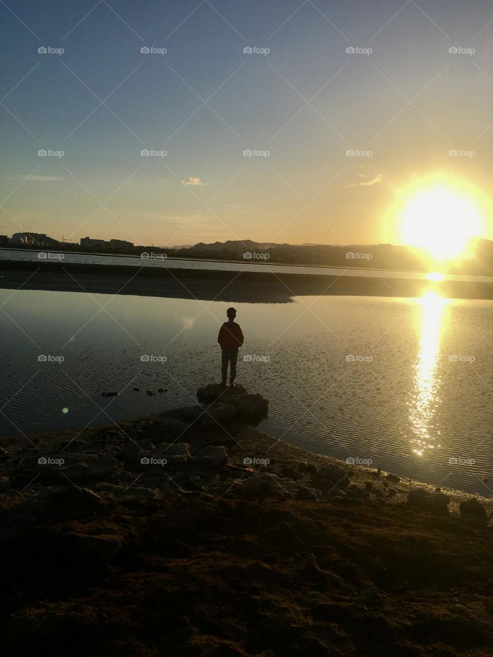 Kid stand on a rock by the lake watching sunset 