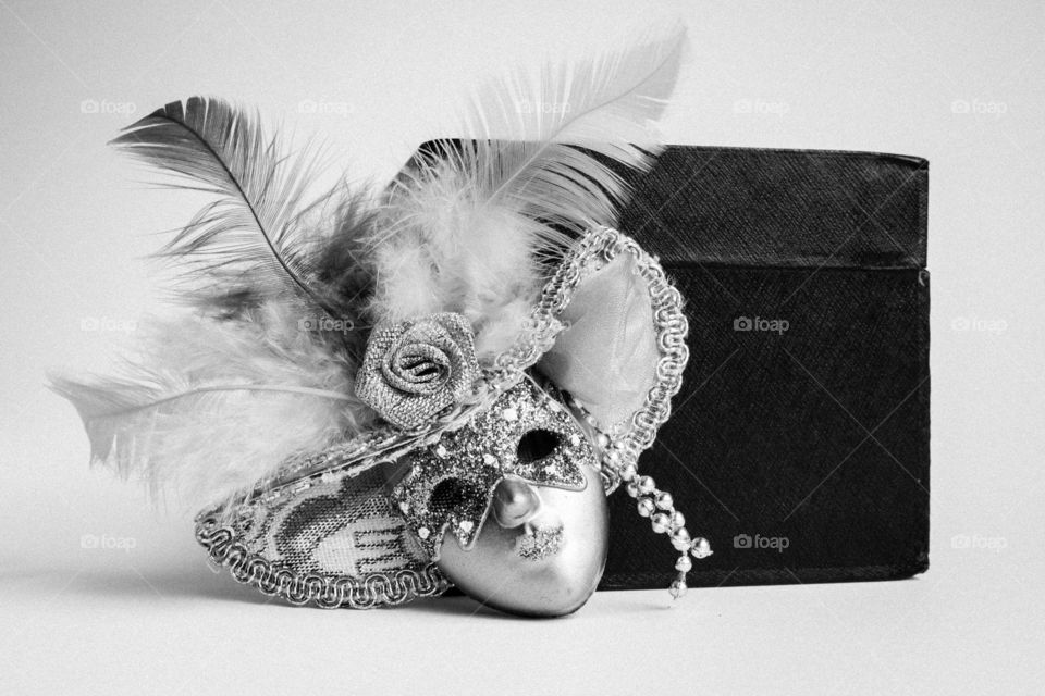 Black and white cube and miniature decorative mask isolated with artificial feathers and textile textures artistic macro shot