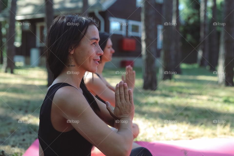 a girl in a black tracksuit, on a pink rug in the forest, does yoga, the girl meditates