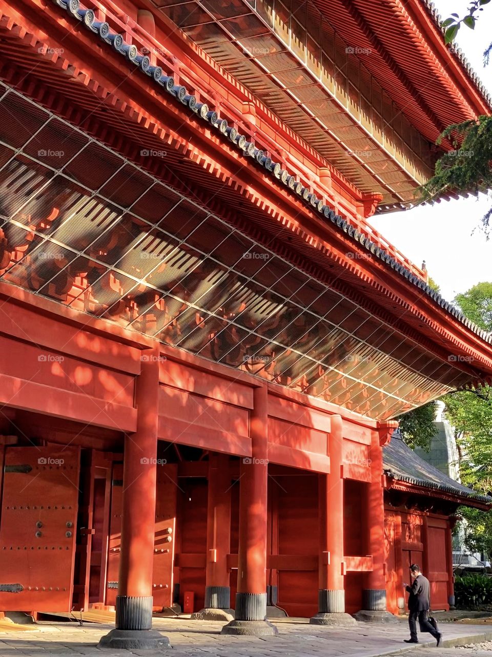 Enormous impressive vermilion red temple gates and busy businessman on his phone at Zojoji Temple in Tokyo.