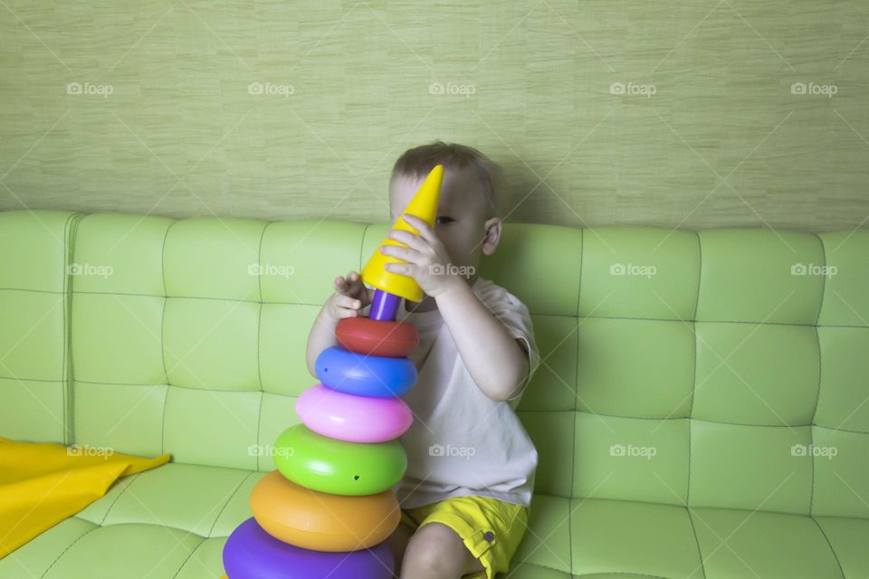 The child is having fun playing a bright pyramid educational toy, sitting on a green sofa.