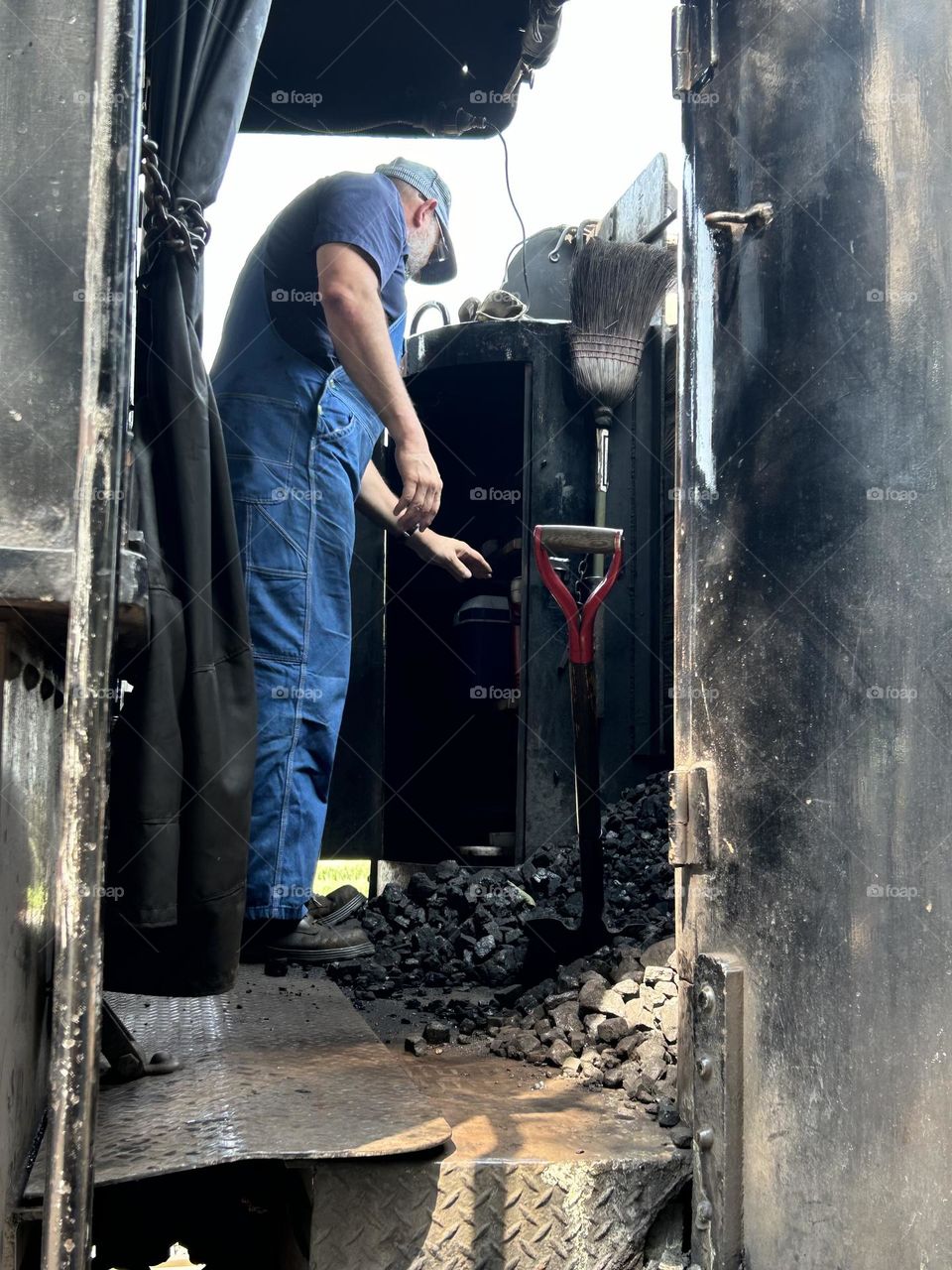 Train conductor standing inside steam engine near coal bin