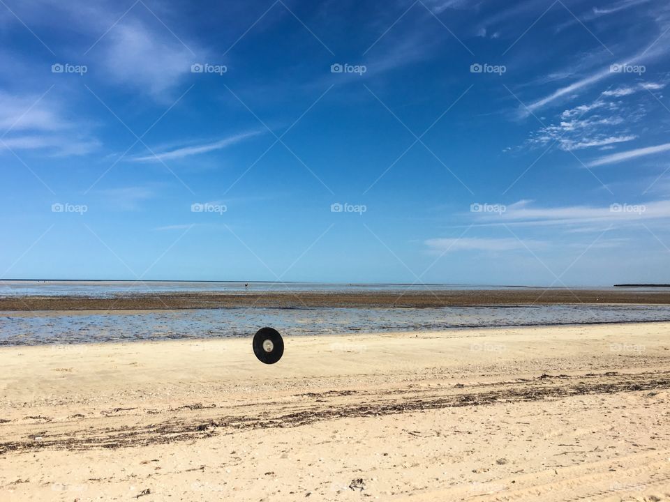 Vintage vinyl music record flying in air rolling down secluded tropical beach at low tide
