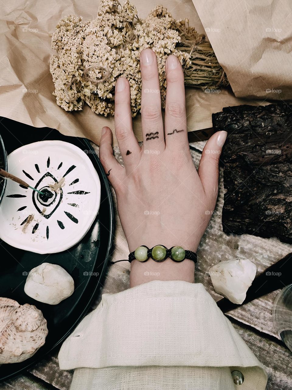 Meditation with herbs, minerals and aromatic sticks. Woman's hand in stone bracelet, magical symbols on fingers