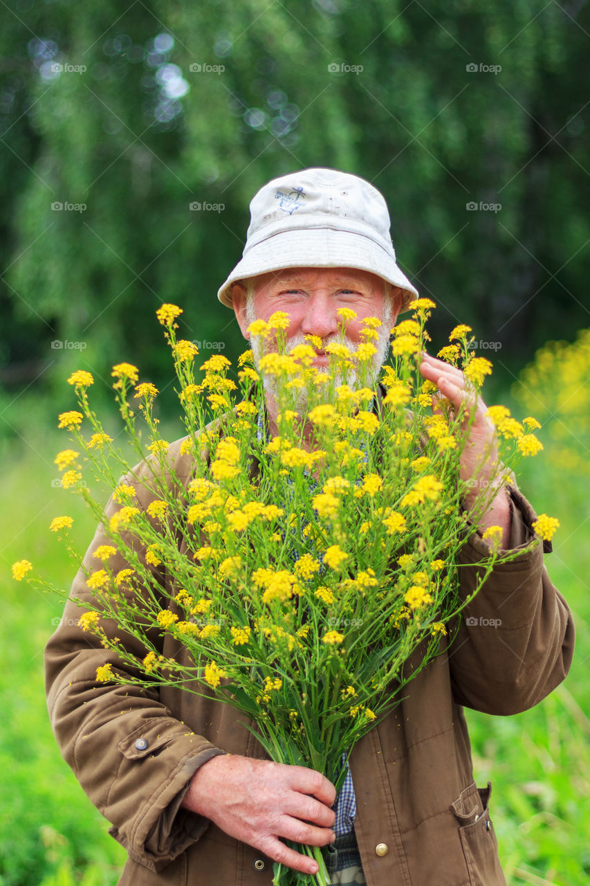 Senior man holding yellow flower in field