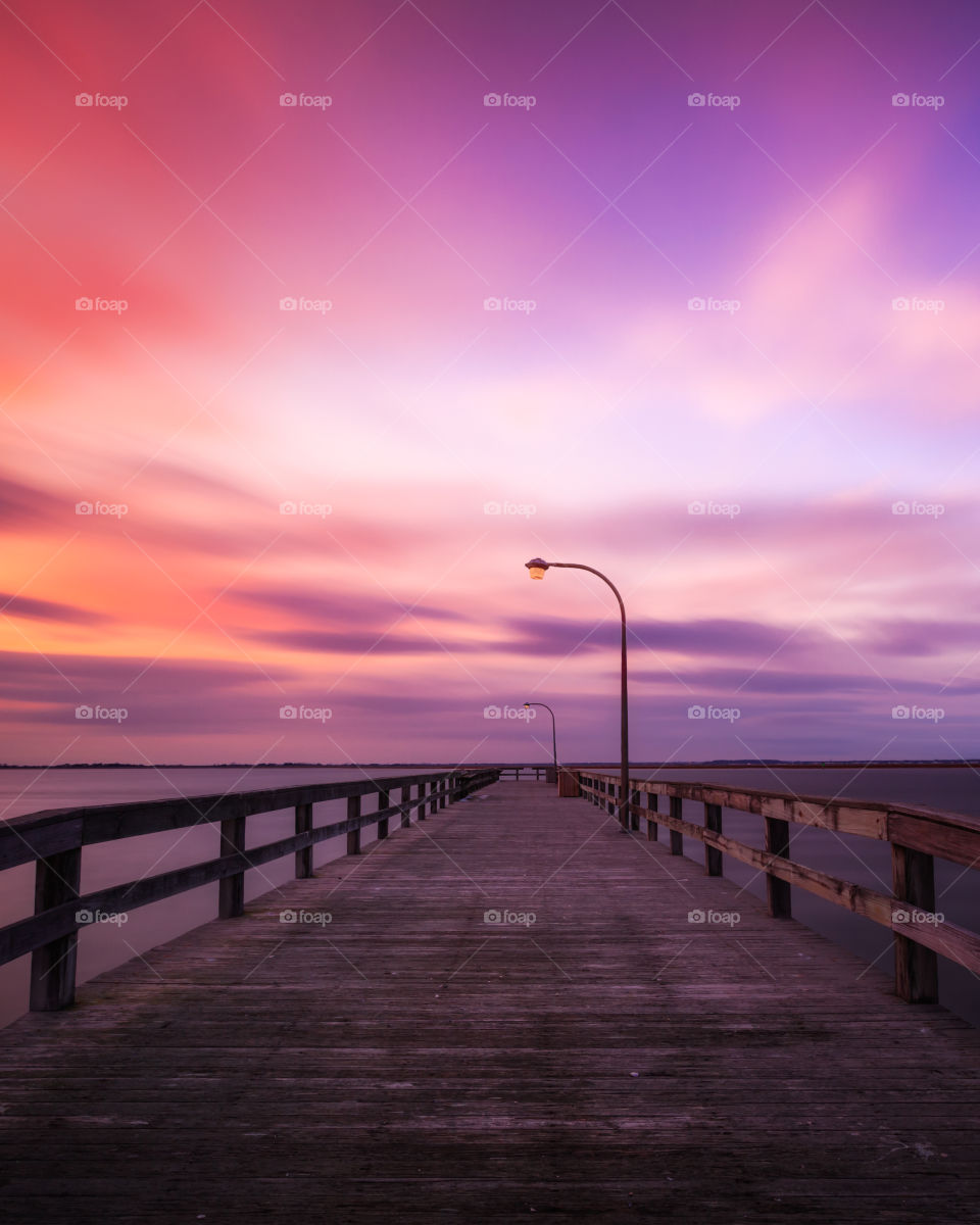 Soft pastel colors in the sky following a sunset over an empty fishing pier on the water. 