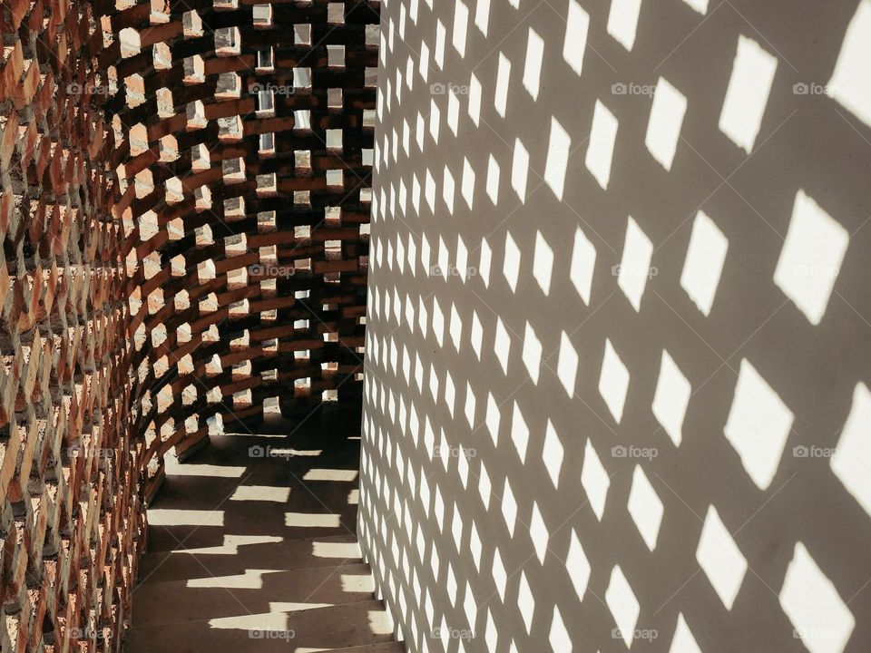 Strong evening lights casting shadows of the perforated brickwall into the passage wall
