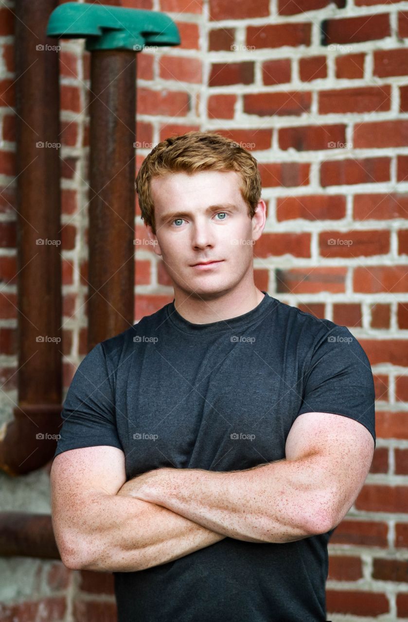 A man with red hair poses in front of a brick wall
