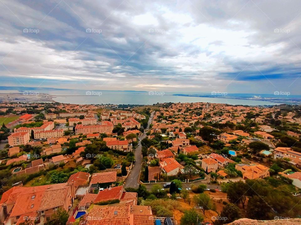 This panoramic view captures the city of Vitrolles, showcasing a sprawling urban landscape with a mix of terracotta-roofed buildings and lush greenery.