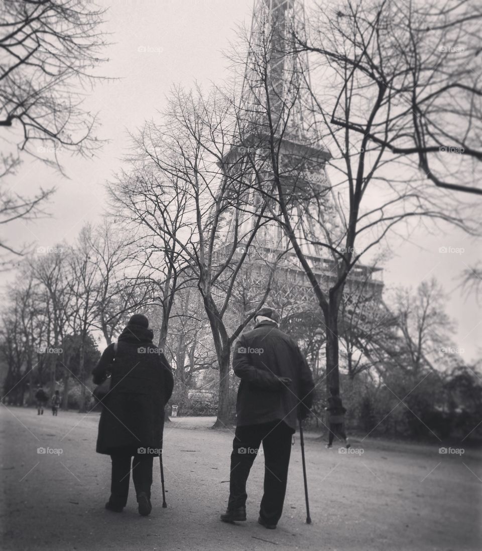 An elderly couple takes a walk together by the Eiffel Tower. Old friends or longtime lovers?