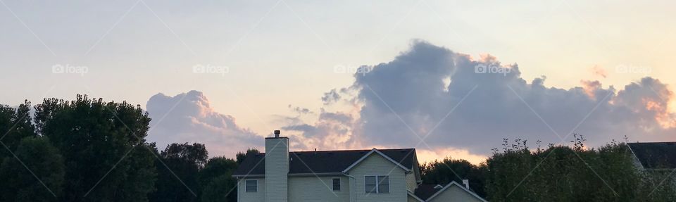 Orange Evening sky during the sunset when sun rays reflect off of the beautiful clouds making them bright and colorful above a suburban house of a neighborhood 