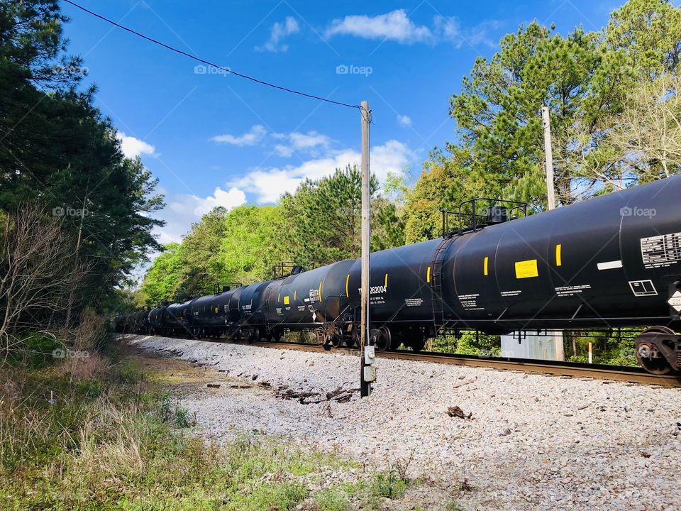 Locomotive tanker cars passing by under a blue sky 