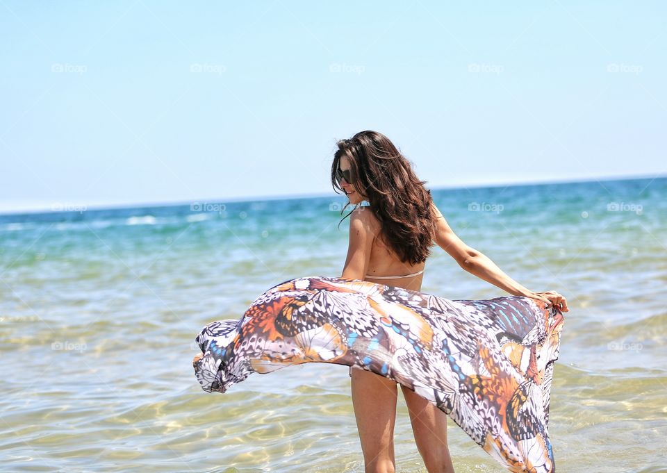Woman in bikini blowing scarf in sea