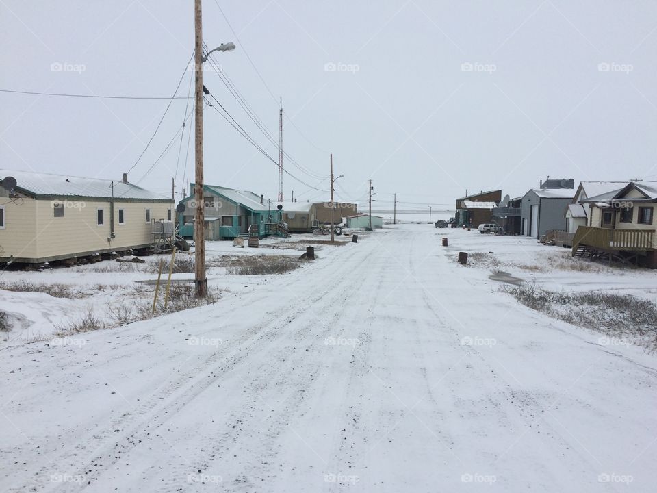 Winter picture of an arctic hamlet road with houses and hydro pole running down one side. 