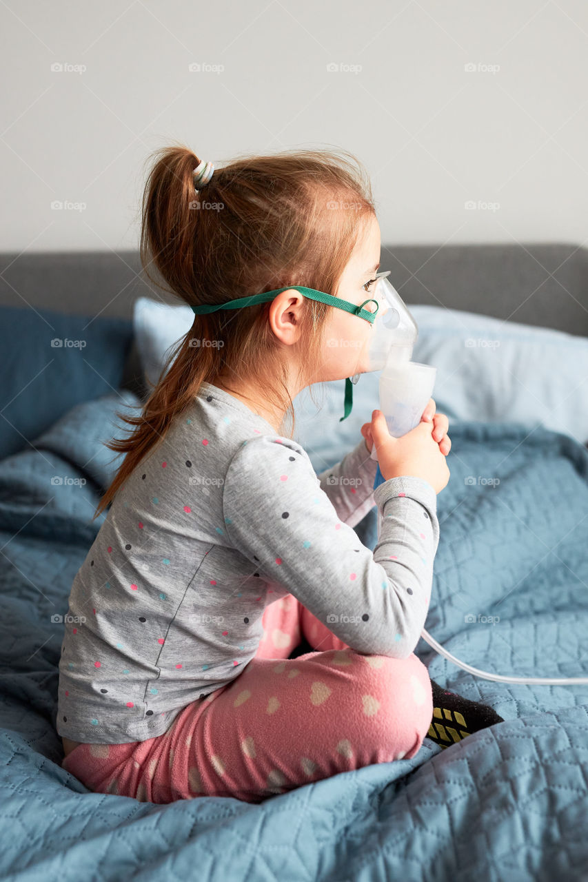 Sick little girl having medical inhalation treatment with nebuliser. Child with breathing mask on her face lying in bed