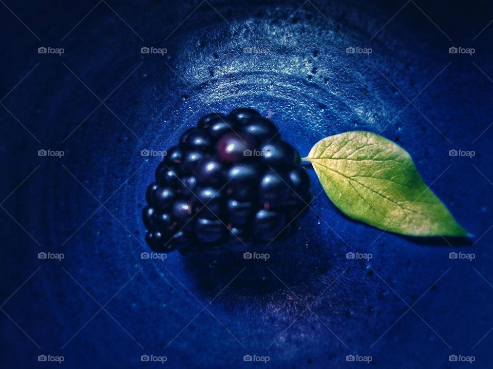 Blackberry with a yellow leaf on a Blue Plate from above