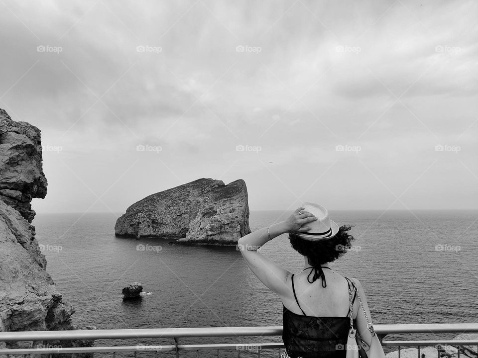 black and white photo of woman from behind with hat looking at the sea