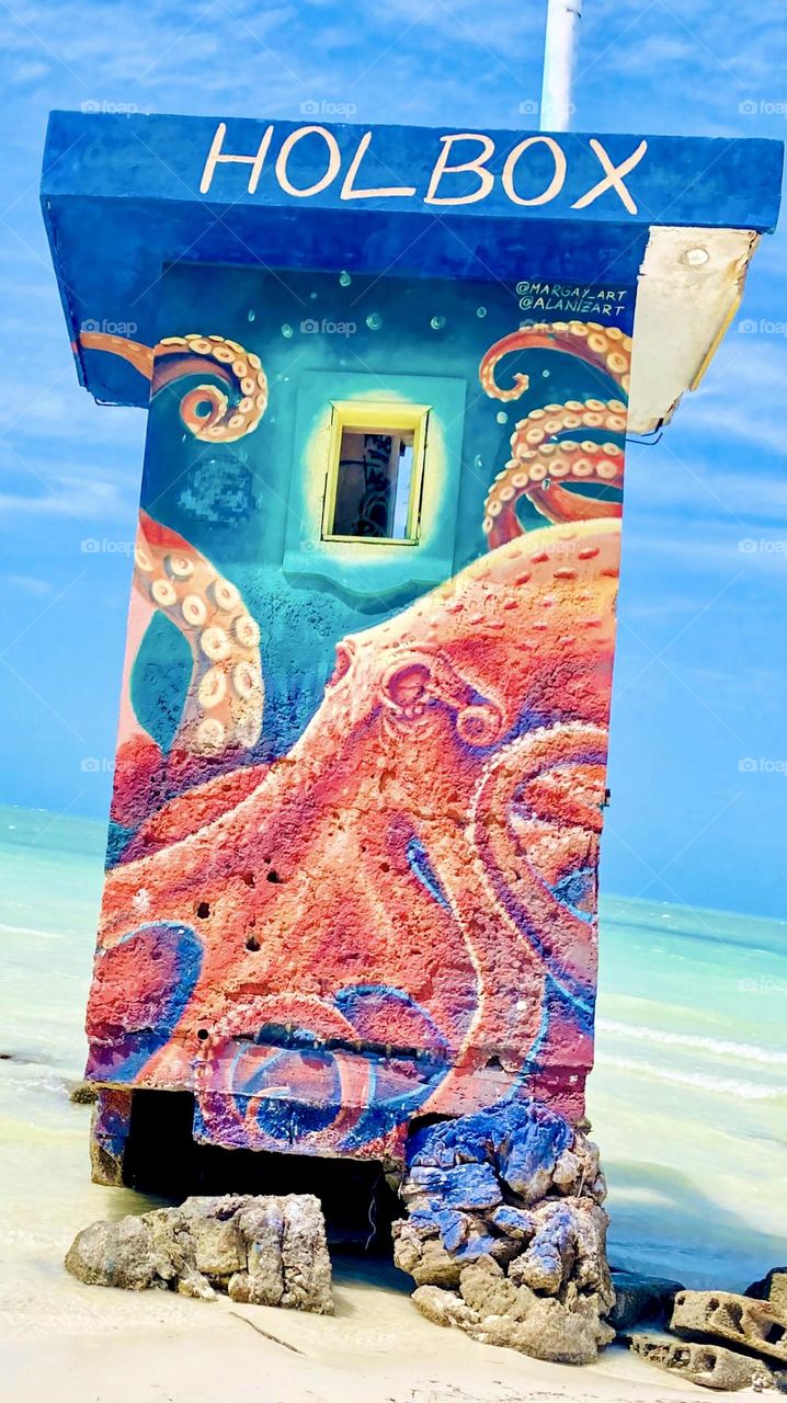 A orangish red octopus painted on a damaged cement pier structure.