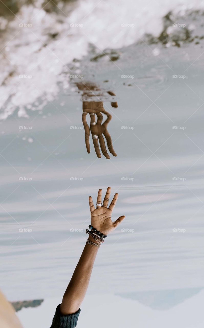 person's hand reaching on water with reflection 