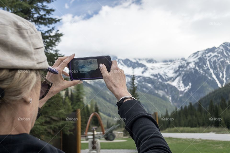 Blonde woman in hat photographing Canadian Rocky Mountain view