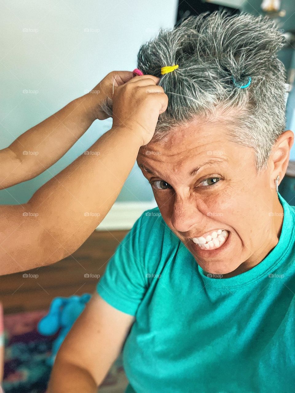 Woman getting hair done by a toddler, toddler puts mommy’s hair in ponytails, tiny pony tails on mommy’s head, woman grimacing from new hairdo, funny hair picture 