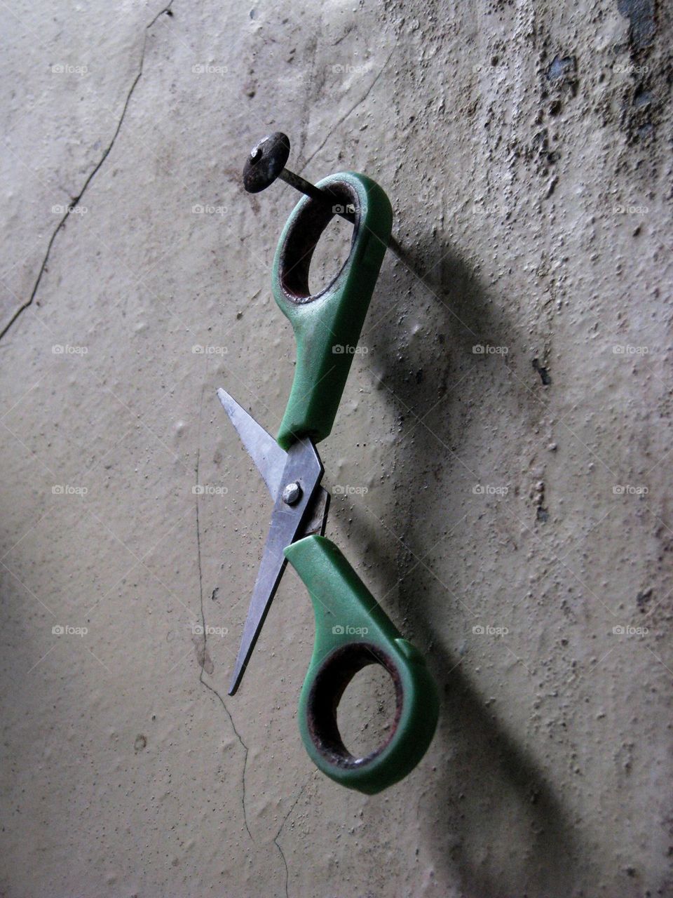 scissors with green handles hanging on a nail on a concrete wall