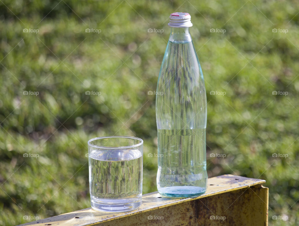 Bottle and glass with fresh  water on grass  background.