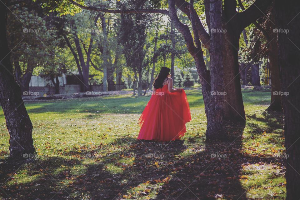 Girl in red dress walking between trees. Mystical