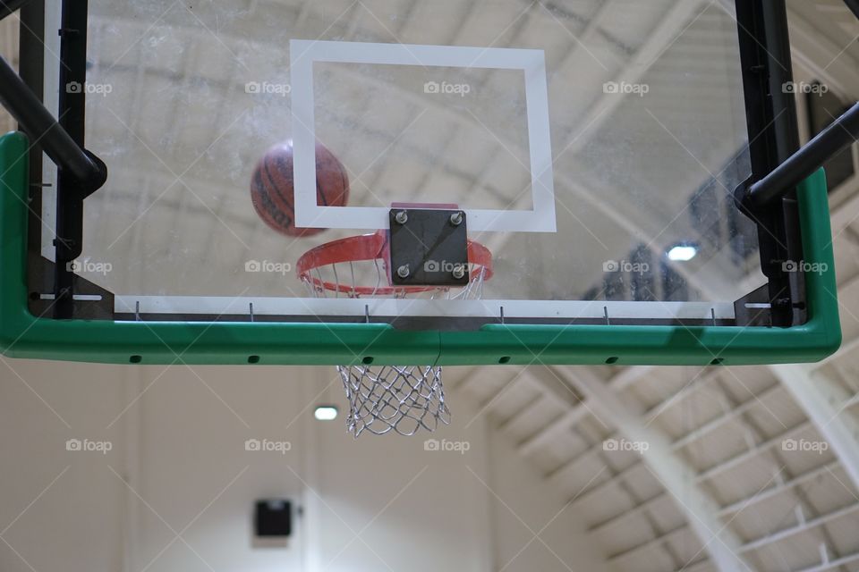 Basketball going into the basket, as seen from behind the clear backboard