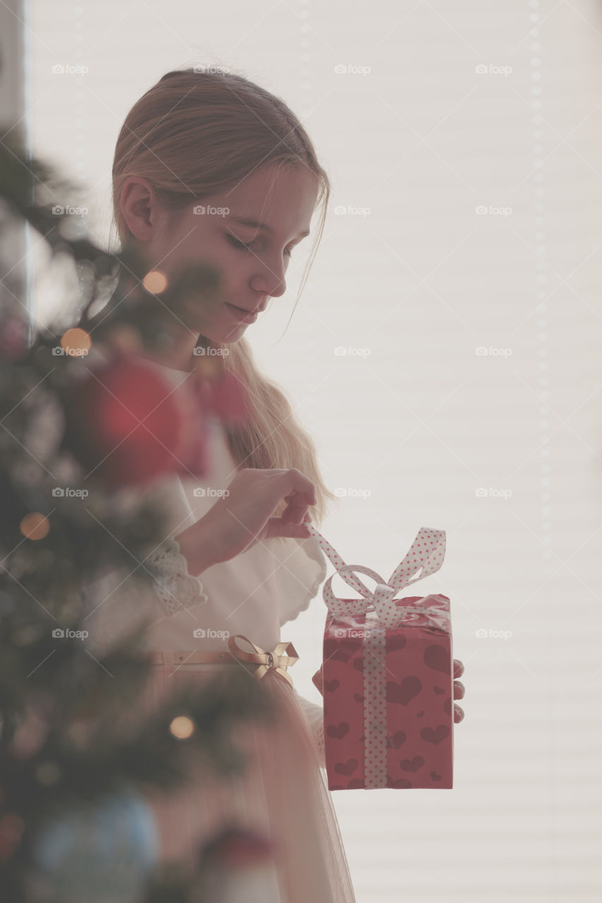 Girl wearing pink dress standing behind a tree and  unpacking Christmas gift