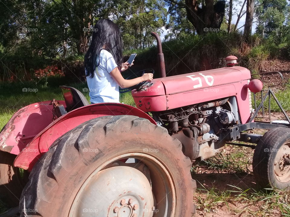 young girl sitting on tractor Massey Ferguson in the field.  Using cell phone Moto G
