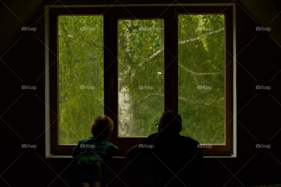 Son and father watching storm through the window.