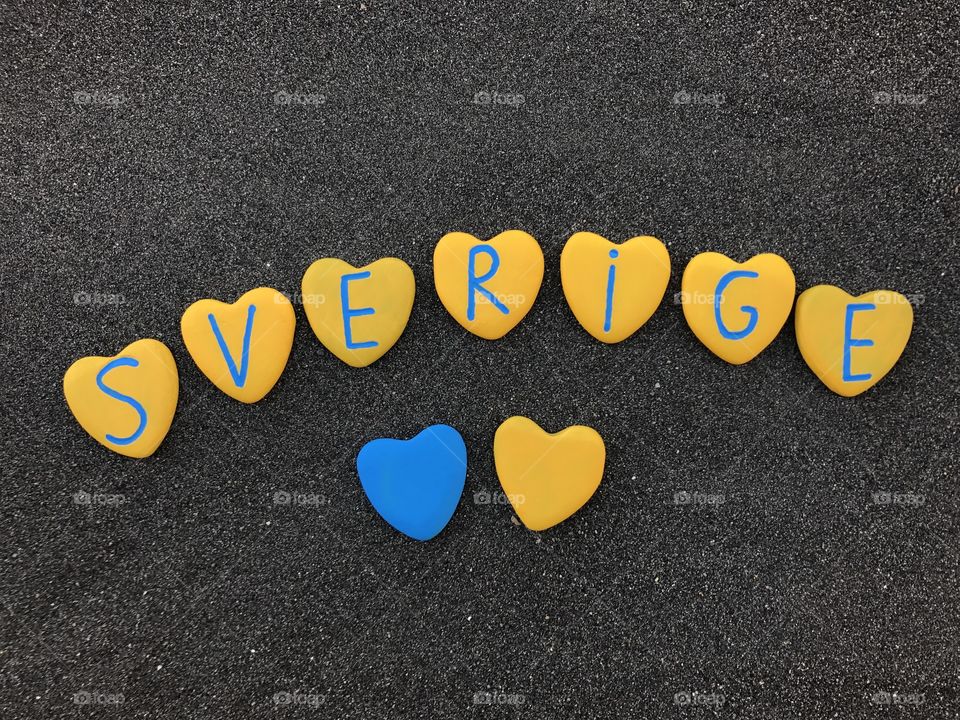 Sverige, Sweden, country name with national colors and heart stones over black volcanic sand 